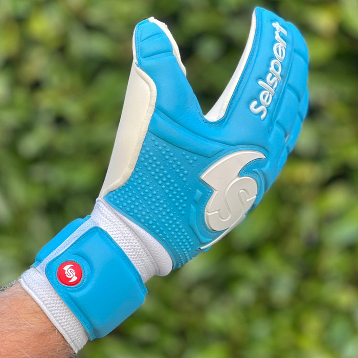 Cyan Selsport goalkeeper glove with white accents on a blurred green background