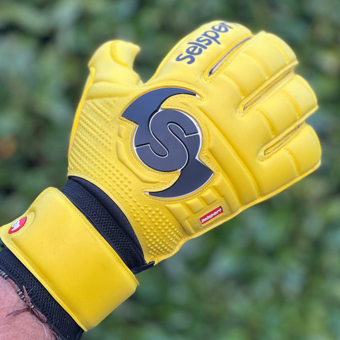 Yellow Selsport Goalkeeper glove with a logo held against a blurred green background