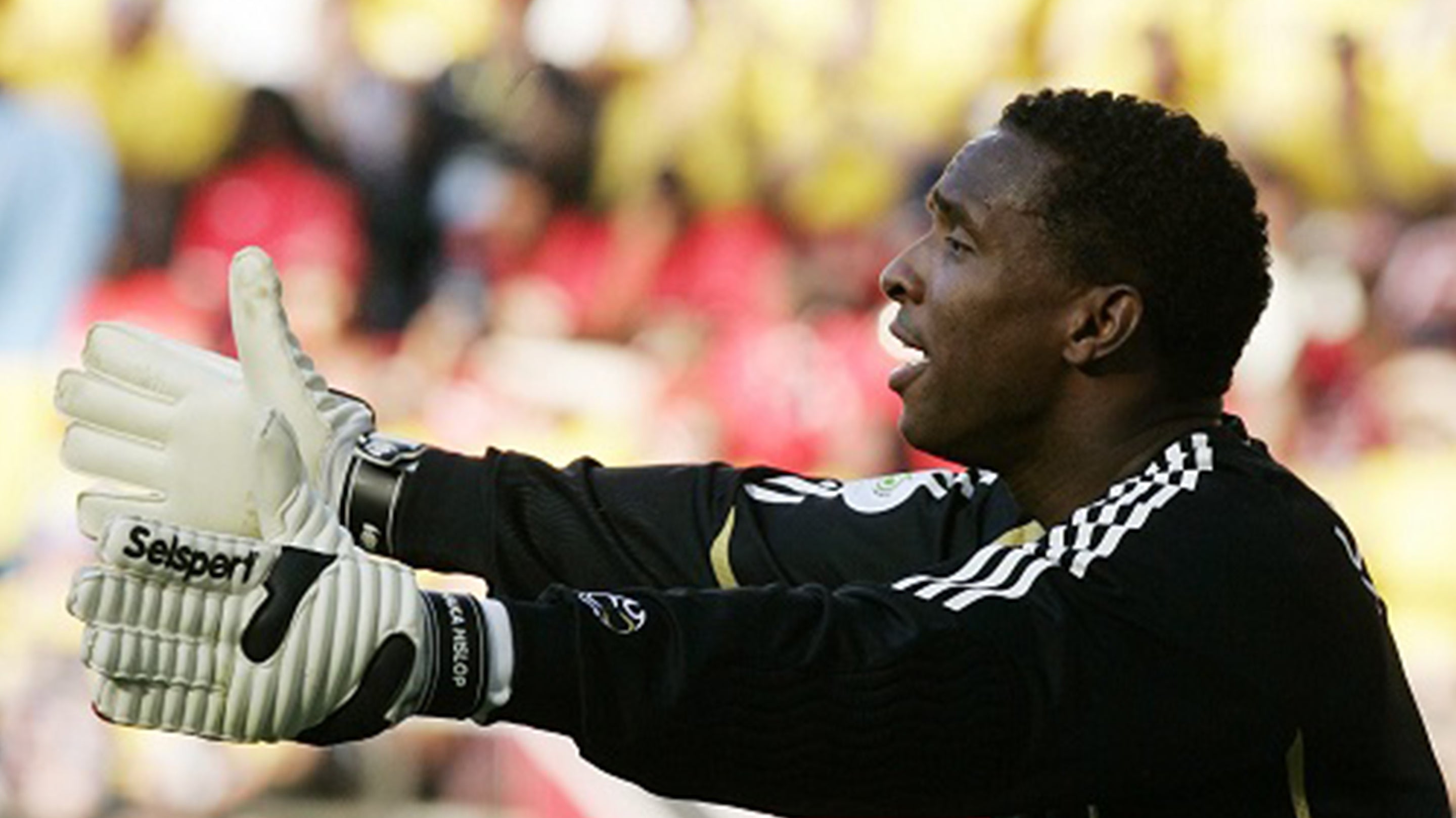 Shaka Hislop International goalkeeper wearing a black goalkeeper shirt with his arms outstretched in Seslport Eurowrap goalkeeper gloves 