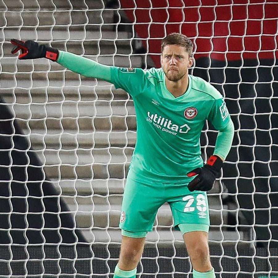 Luke Daniels in Green Brentford goalkeeper kit standing in goal pointing his right arm to the goalpost wearing Selsport Diavolo Rosso Goalkeeper gloves